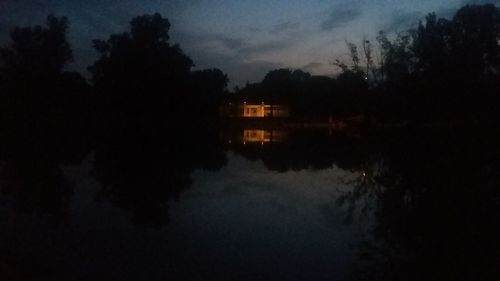 Silhouette trees by lake against sky at night