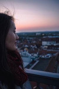 Portrait of woman looking at city against sky during sunset