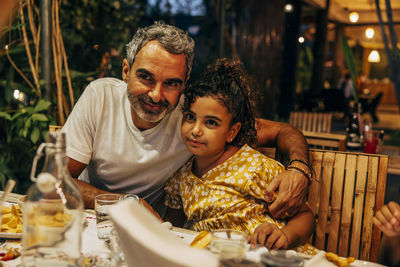 Smiling father with arm around daughter sitting at table in restaurant on vacation