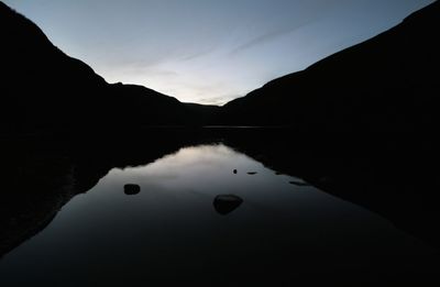 Scenic view of lake by silhouette mountain against sky