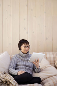 Senior woman using tablet computer while sitting on sofa at home