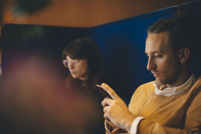 Mid adult businessman using smart phone while sitting by young female colleague at office cafeteria