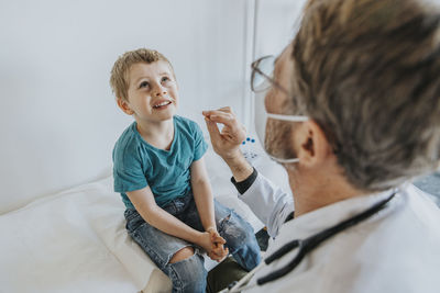 Doctor taking nasal swab test of boy while sitting at clinic