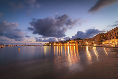 Illuminated buildings by sea against sky