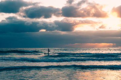 Silhouette man surfboarding on sea against cloudy sky during sunset