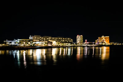Illuminated city by river against clear sky at night