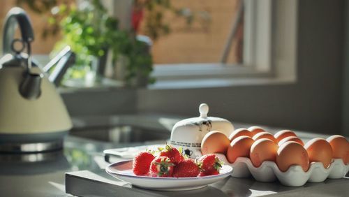 Eggs in carton by strawberries and tea kettle at table