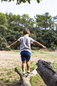 Rear view of boy walking fallen tree in forest