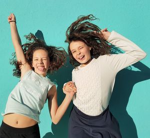 Happy friends with long hair against wall on sunny day