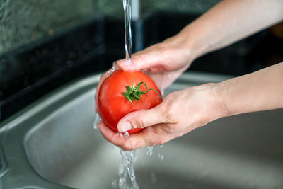 Girl washes fresh tomato over sink, close-up