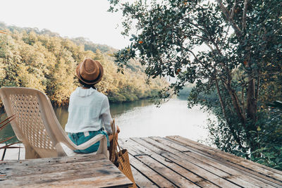 Rear view of man sitting on chair by lake