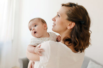 Happy mother carrying adorable baby at home