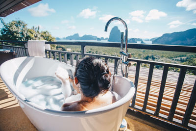 Woman bathing in bathtub by railing