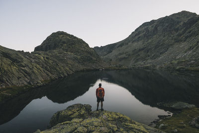 Rear view of man standing on mountain by lake against sky