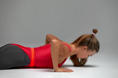 Side view of woman doing push ups against gray background