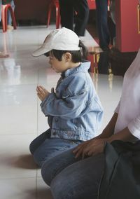 Side view of boy praying while kneeling on tiled floor in temple