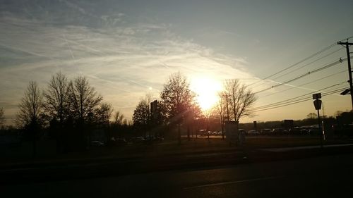 Road by trees against sky during sunset