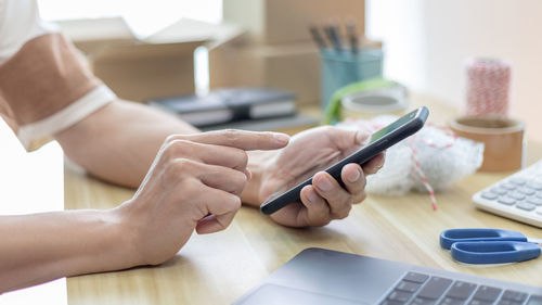 Cropped hands of woman using mobile phone on table