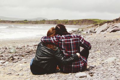 Rear view of couple standing on beach against sky