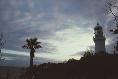 Silhouette palm trees and lighthouse against sky at sunset