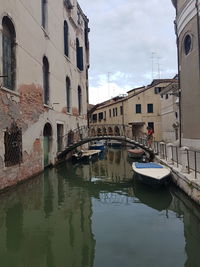 Boats moored in canal amidst city against sky