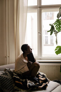 Thoughtful young woman with book sitting on bed at home