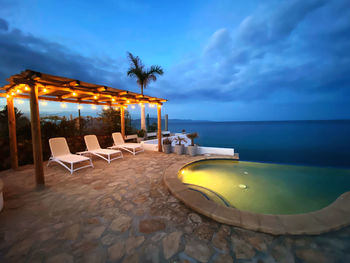 Lounge chairs by swimming pool at beach against sky