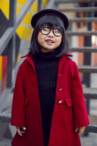 Korean girl in a red coat and cap and round glasses stands on the iron staircase the street 