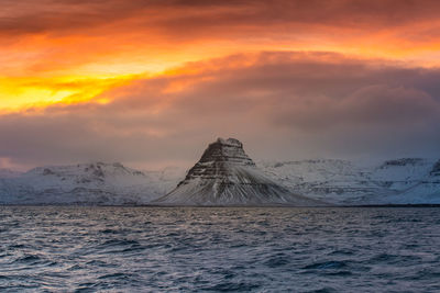 Scenic view of sea by snowcapped mountains against sky during sunset