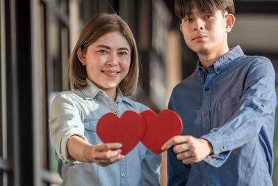 Portrait of smiling couple holding heart shape while standing outdoors