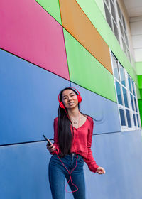 Full length of a smiling young woman standing against wall