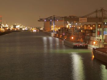 Boats moored on river against illuminated city at night