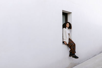 Young woman with afro hair sitting on window sill of building