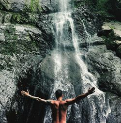 Rear view of shirtless man standing on rock