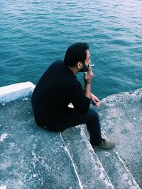 Young man using mobile phone while sitting by sea