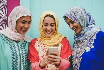 Smiling female friends using smart phone against wall