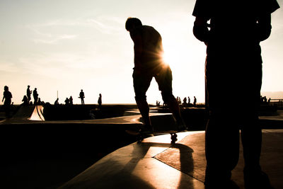 Silhouette people at skateboard park against sky during sunset