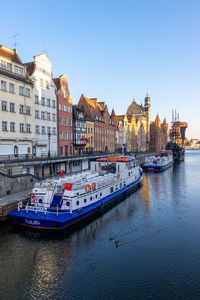 Boats moored on river by buildings against sky