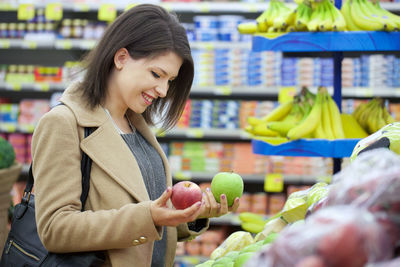Side view of smiling young woman holding apples in store