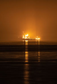 Illuminated ship in scenic sea against sky at sunset