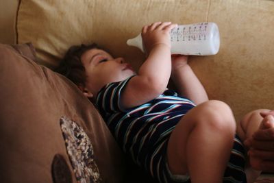 Baby boy having milk while lying on sofa at home