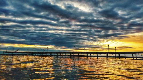 Silhouette bridge over river against dramatic sky