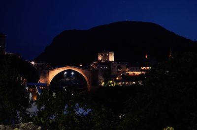 Illuminated arch bridge and buildings against sky at night