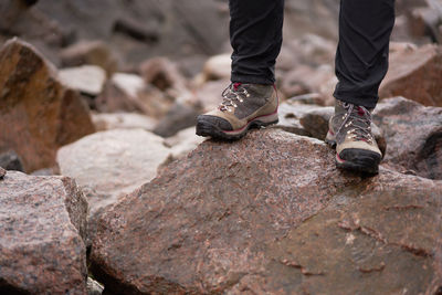 Legs of crop unrecognizable explorer in trekking boots standing on rough boulders during adventure