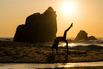 Silhouette woman doing yoga on  beach against sky during sunset