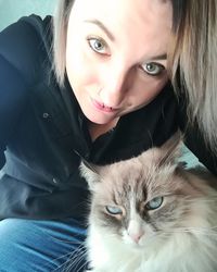 Close-up portrait of smiling young woman with cat sitting at home