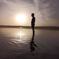 Silhouette man standing in sea against sky during sunset