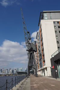 Cranes at pier amidst buildings in city against sky