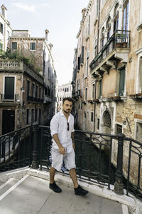 Full length of man walking by railing on bridge over canals amidst residential building