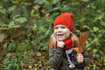 Portrait of a girl in an orange hat with an autumn leaf against the background of the forest